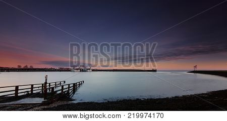 Looking over a slipway to your left at two ferries in a cove with a flat sea under a blue-orange dawn
