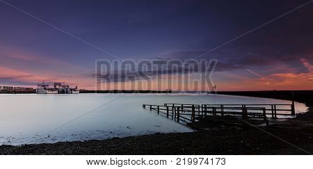 Looking over a slipway to your right at two ferries in a cove with a flat sea under a blue-orange dawn