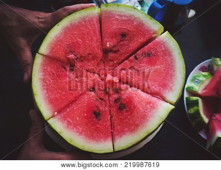 Man cuts red juicy ripe watermelon in slices with knife on dark background slowmotion. Slices of watermelon closeup