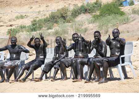 DEAD SEA, JORDAN, April. 18, 2014. a group of African young men taking mud bath in the sun at the beach of Dead Sea.