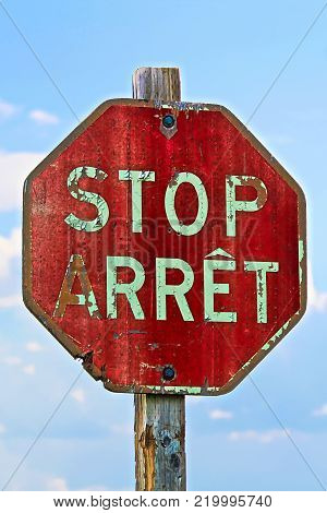 An old stop sign in both french and english against a blue sky.
