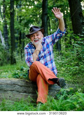 Hello. Mature Man With Beard In Cowboy Hat. Farmer Sit On Wood. Happy Forester. Human And Nature. Hi