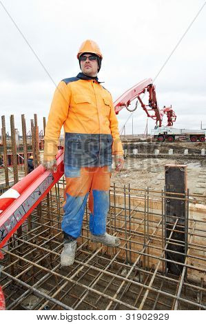 operaio Builder in piedi vicino a pompa calcestruzzo carrellato boom sul rinforzo di bacchette di metallo di Cement