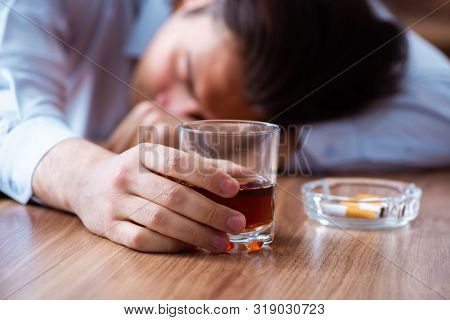 Male employee drinking alcohol and smoking cigarettes at workpla