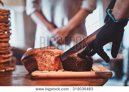 Man In Gloves Is Slicing Tasty Loaf For Lunch At Small Artisan Caffeteria.