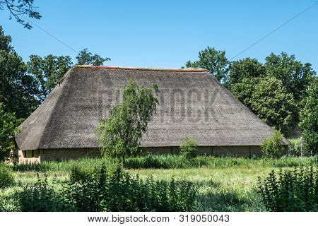 Bokrijk, Belgium - June 27, 2019: Giant Barn With Gray Straw Roof Is Set In Green Of Meadow And Surr