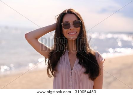 Portrait Of Beautiful Smiling Girl In Sunglasses And Pink Dress At Calm Seaside.
