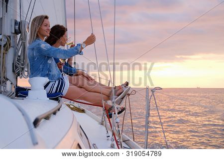 Two Joyful Women Are Celebraiting Good Summer Day At The Yacht While Watching Beautiful Sunset.