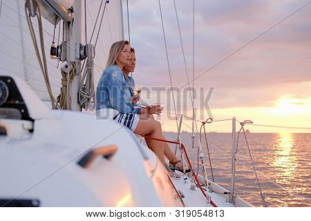 Two Joyful Women Are Celebraiting Good Summer Day At The Yacht While Watching Beautiful Sunset.