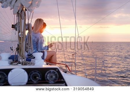 Two Joyful Women Are Celebraiting Good Summer Day At The Yacht While Watching Beautiful Sunset.