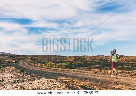 Fitness training in outdoor landscape volcano. Athlete woman running on trail run path in volcanic background at sunset.
