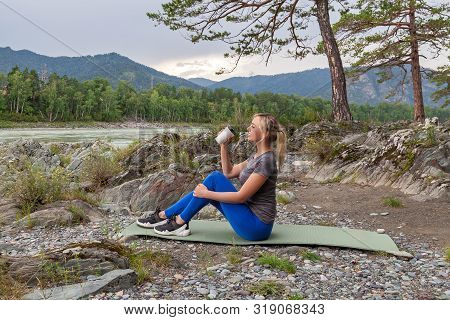 Blond Beautiful Girl Sitting On The Mat On The Stone Ground Drinking Coffee Or Tea, Resting After Sp