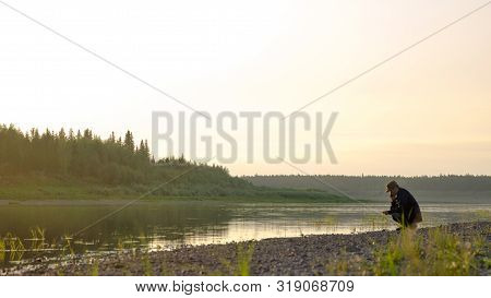 Male Yakut Squat Incline Of The Head Talking On The Mobile Phone On The Shore Of The Wild North Of T