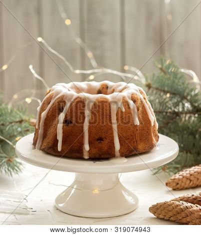 Pie With Raisins And Icing From Powdered Sugar On The Background Of Fir Branches And Garlands. Rusti