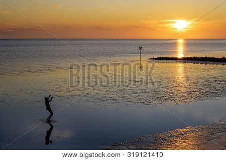 Little Boy As Silhouette Is Looking Into The Setting Sun On The Beach Of The North Sea At Low Tide ,