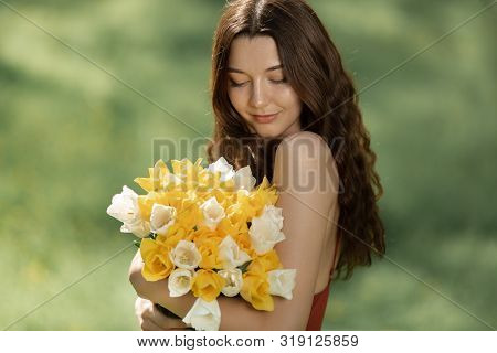 Attractive Woman In Red Dress With A Bouquet Of Spring Flowers Against Nature Bokeh Green Background