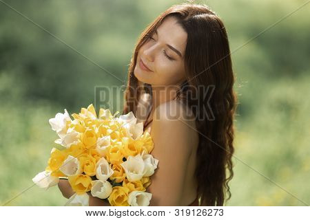 Attractive Woman In Red Dress With A Bouquet Of Spring Flowers Against Nature Bokeh Green Background