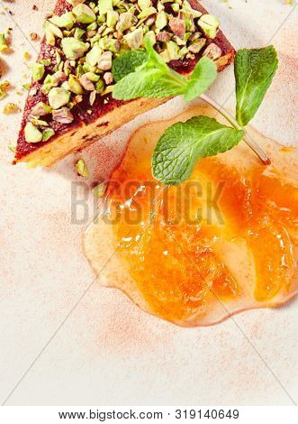 Healthy nut cake with apricot jam isolated on white background. Slice of walnut carrot sponge cake decorated with pistachios and fruit confiture on white round plate for restaurant menu