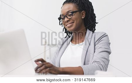 Entrepreneurship Concept. Positive Afro Businesswoman Working On Laptop At Wokplace. Empty Space