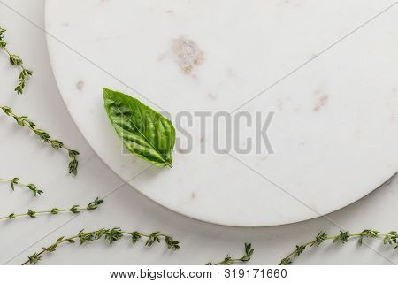 Top View Of Round Marble Surface With Basil Leaf Near Thyme Twigs On White Background