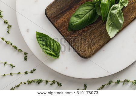 Top View Of Round Marble Surface With Brown Wooden Cutting Board And Basil Bundle Near Thyme Twigs O