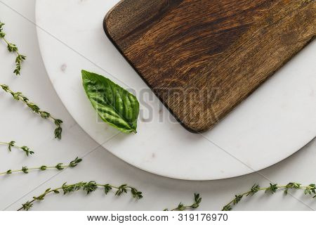 Top View Of Round Marble Surface With Brown Wooden Cutting Board And Basil Leaf Near Thyme Twigs On 