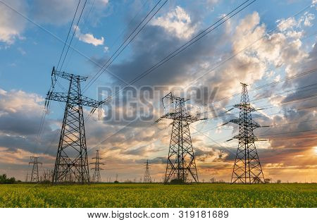 Power Lines And High-voltage Lines Against The Backdrop Of Blooming Oilseed Rape On A Summer Day. Gr