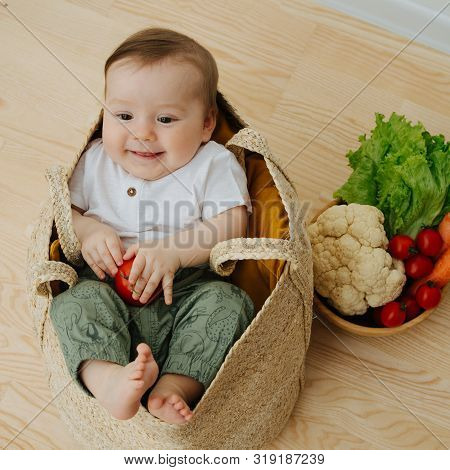 Infant Baby In A Woolven Like Bag And Bowl Of Vegetables Nearby