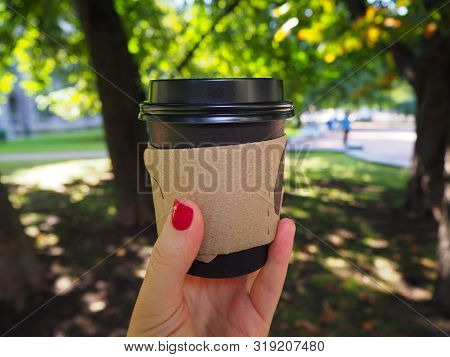 Disposable Black Paper Coffee Cup In Woman Hand With Red Manicure On The Park Background. Eco Friend