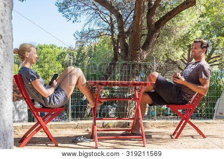 Couple On Vacations Resting In Front Of Bungalow House At Camping Site In Pure Nature. Family Vacati