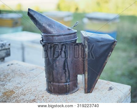 Beekeeper Smoker Smokes White Smoke. Apiary Background. Beekeeping Tool Close Up. Smoker Stands On T