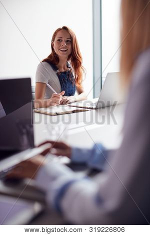Two Casually Dressed Young Businesswomen Working On Laptops In Modern Meeting Room