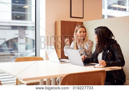 Two Young Businesswomen In Meeting Around Table In Modern Open Plan Workspace