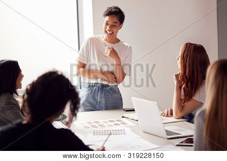 Female Boss Gives Presentation To Team Of Young Businesswomen Meeting Around Table In Modern Office