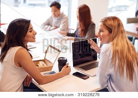 Group Of Young Businesswomen Sitting Around Table In Modern Workspace Having Working Lunch Meeting
