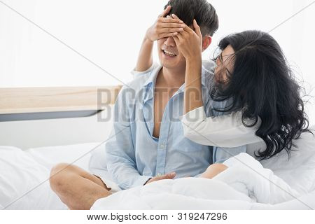 Asian Couple Sitting On The Bed Together, Woman Blindfolded Boyfriend.