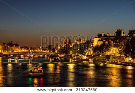 Nightfall Over Seine River And Illuminated Pont Des Arts With Palais Royal And Musee Dorsay In Backg