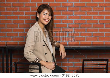 Image Of Smiling Long Brown Hair Asian Businesswoman Standing At Coffee Coner With Brown Bricks Wall