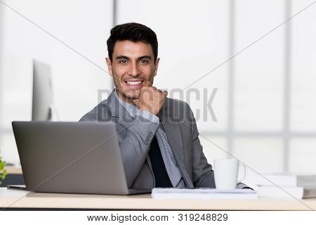 Smiling Handsome Caucasian Businessman In Black Suit Support The Chin In Modern Office.