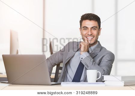 Smiling Handsome Caucasian Businessman Touch His Wrist, There Is Notebook Computer On Table In Moder