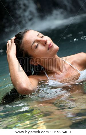 Beautiful woman enjoying bathing near natural waterfall