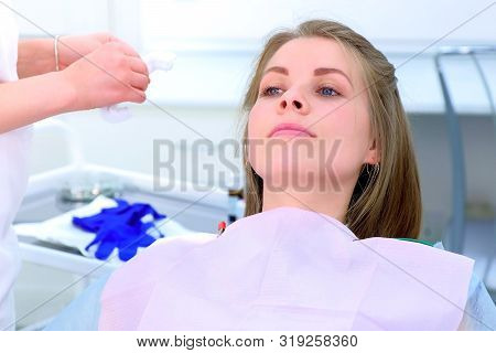 Dentist Nurse Prepares Woman Patient To Teeth Cure In Dentistry Clinic. She Puts Cap And Napking On 