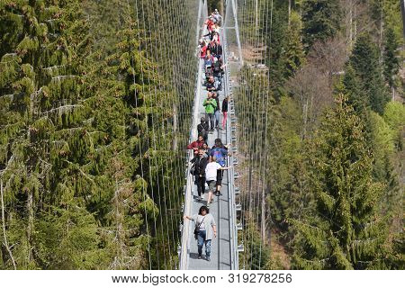 Bad Wildbad, Germany - April 22, 2019: Tourists Walk Along A Long And Suspended Iron Cable Bridge Fo