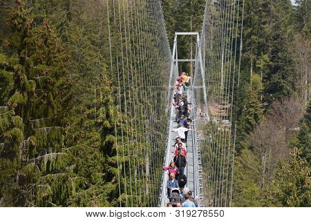 Bad Wildbad, Germany - April 22, 2019: Tourists Walk Along A Long And Suspended Iron Cable Bridge Fo