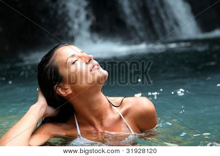 Beautiful woman enjoying bathing near natural waterfall
