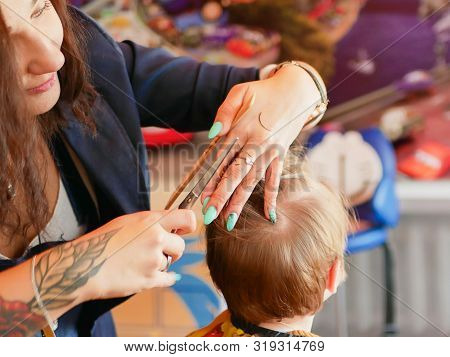 First Baby Haircut. Cute Blonde Toddler Is Happy To Be On A Haircut With A Professional Baby Hairdre