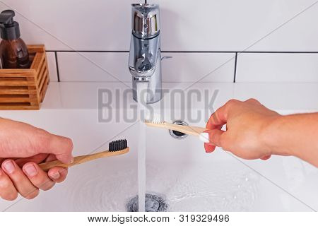 Mans And Womans Hands Close-up Holding A Bamboo Toothbrush Near The Water Tap