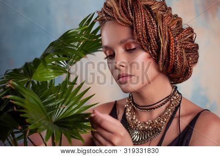 Southern Flavor. A Young Tanned Woman With Afro Braids Smiles Holding A Big Pot With A Tropical Plan