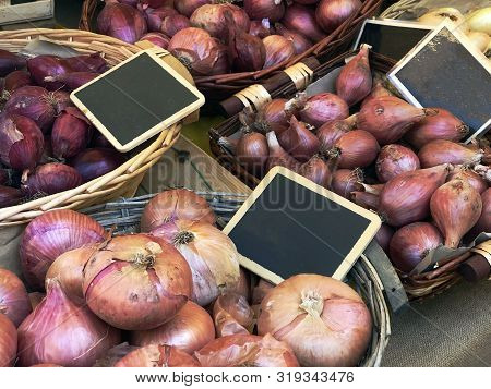 Red Onions In Baskets With Boards Selling On Market