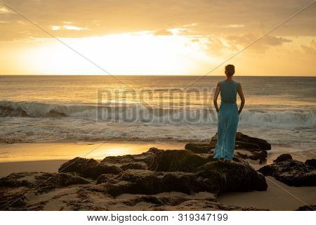 Woman Enjoying Sunset At The Beach. View From Back. Golden Sunset. Sunset Seascape. Bright Sunlight.